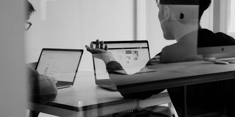 Two people reviewing figures on laptops in a meeting room